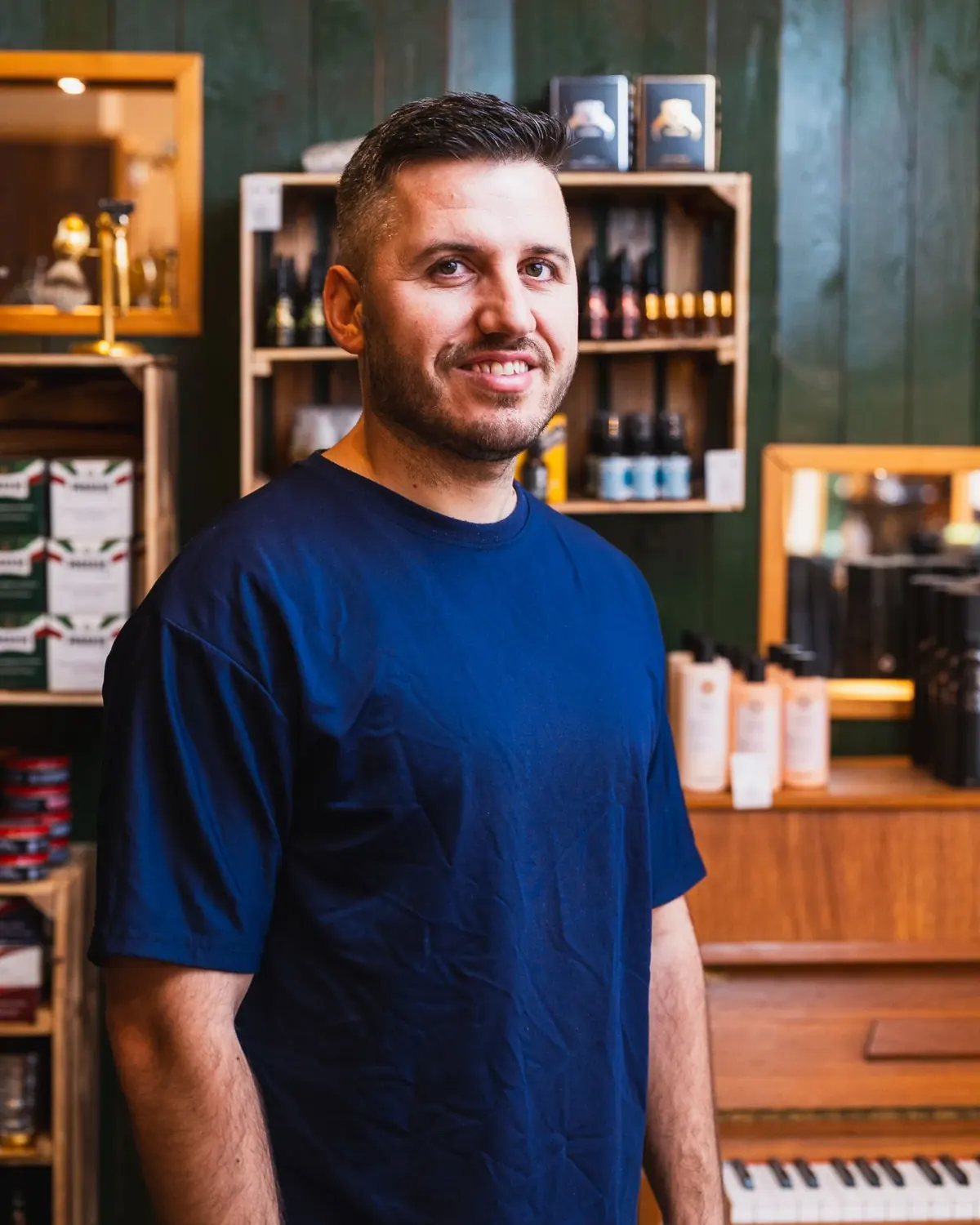 Portrait of Wilson smiling in front of grooming product shelves at a Malmö barbershop