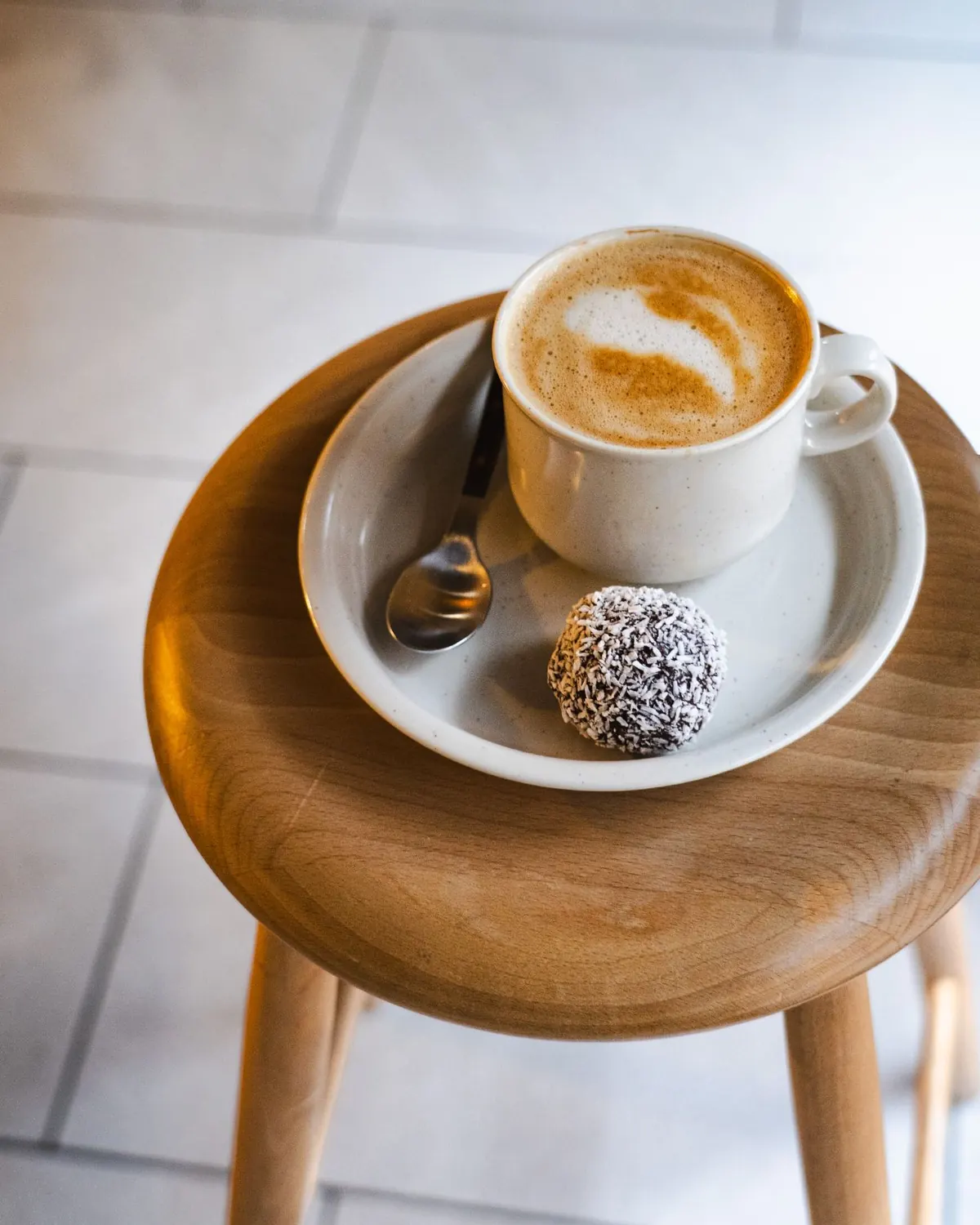 A latte and a coconut-covered chocolate ball on a plate