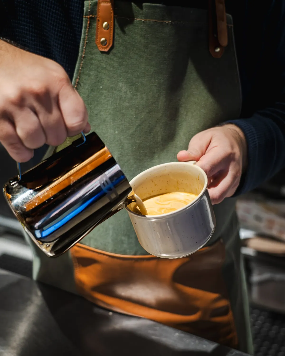 A barista pouring steamed milk into a cup of coffee